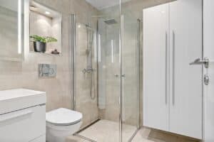 Baño de hotel con mampara de ducha de vidrio transparente y perfilería cromada en espacio minimalista