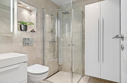 Baño de hotel con mampara de ducha de vidrio transparente y perfilería cromada en espacio minimalista