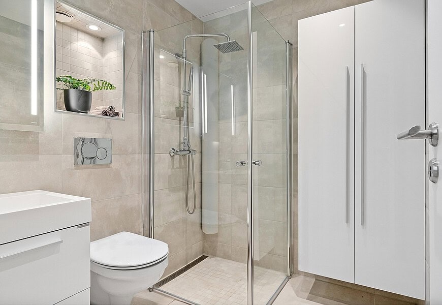 Baño de hotel con mampara de ducha de vidrio transparente y perfilería cromada en espacio minimalista