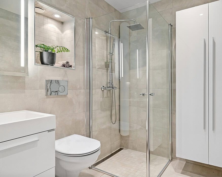 Baño de hotel con mampara de ducha de vidrio transparente y perfilería cromada en espacio minimalista