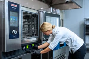 Cocinera insertando cartucho de limpieza en horno combinado RATIONAL iHexagon en cocina profesional