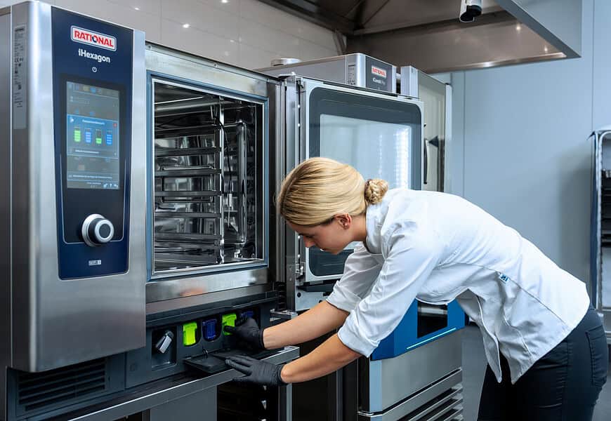 Cocinera insertando cartucho de limpieza en horno combinado RATIONAL iHexagon en cocina profesional