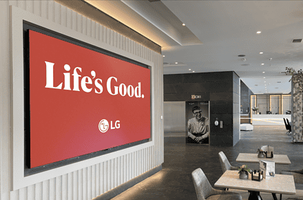 Pantalla LED de LG con campaña Life's Good instalada en el lobby de un hotel moderno con zona de recepción al fond