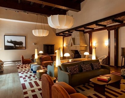 Salón del Parador de Olite-Erriberri renovado, con mobiliario contemporáneo en tonos burdeos y miel, vigas de madera y chimenea de piedra original