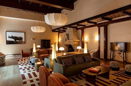 Salón del Parador de Olite-Erriberri renovado, con mobiliario contemporáneo en tonos burdeos y miel, vigas de madera y chimenea de piedra original