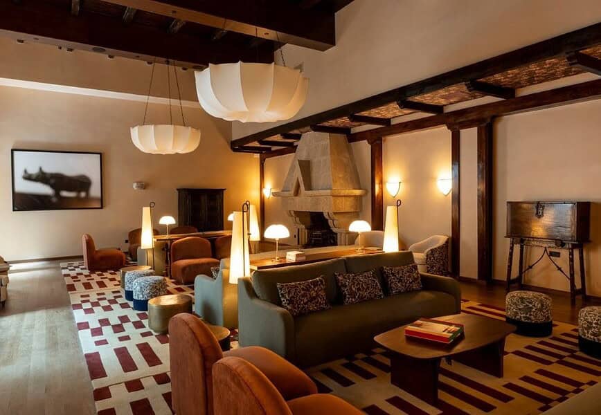 Salón del Parador de Olite-Erriberri renovado, con mobiliario contemporáneo en tonos burdeos y miel, vigas de madera y chimenea de piedra original