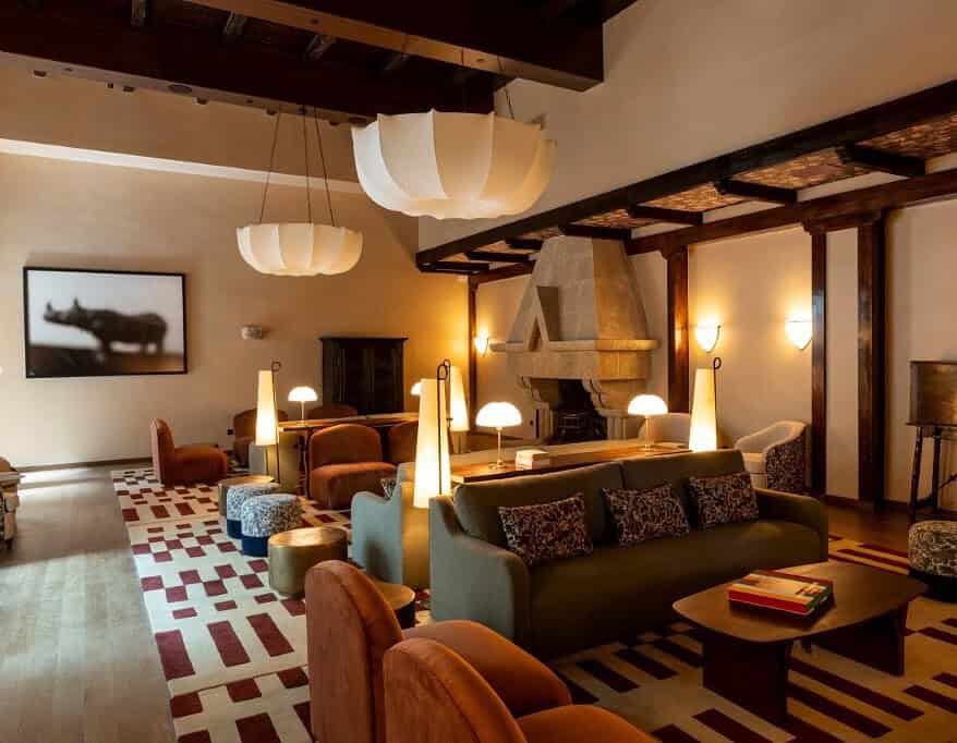 Salón del Parador de Olite-Erriberri renovado, con mobiliario contemporáneo en tonos burdeos y miel, vigas de madera y chimenea de piedra original