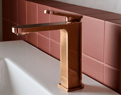 Grifo monomando Roca Kay en acabado cobre cepillado sobre lavabo blanco en baño de diseño contemporáneo con pared de microcemento y azulejos rosas