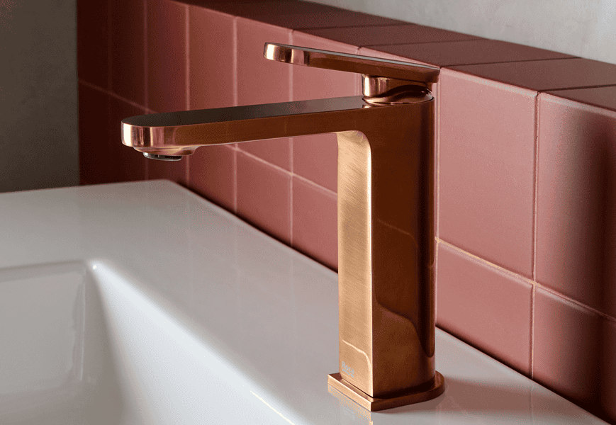 Grifo monomando Roca Kay en acabado cobre cepillado sobre lavabo blanco en baño de diseño contemporáneo con pared de microcemento y azulejos rosas