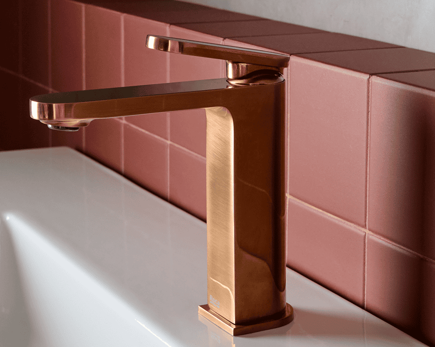 Grifo monomando Roca Kay en acabado cobre cepillado sobre lavabo blanco en baño de diseño contemporáneo con pared de microcemento y azulejos rosas