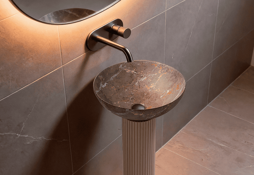 Lavabo de sobremesa Bathco New Lys con acabado Mármol Gris Oro sobre pedestal acanalado en baño de diseño con espejo retroiluminado