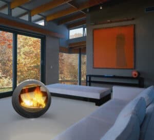 (chimenea Eclypsya en salón) Chimenea de leña nómada Arkiane modelo Eclypsya de diseño circular en salón contemporáneo con vistas al jardín otoñal