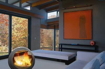 (chimenea Eclypsya en salón) Chimenea de leña nómada Arkiane modelo Eclypsya de diseño circular en salón contemporáneo con vistas al jardín otoñal